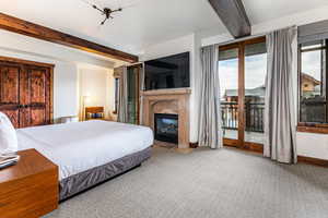 Primary Bedroom featuring beamed ceiling, a glass covered fireplace, access to outside, and carpet flooring
