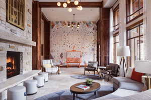 Living room featuring a stone fireplace, a towering ceiling, a chandelier, and stone tile floors