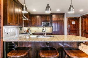 Kitchen featuring light stone counters, a breakfast bar, a peninsula, tasteful backsplash, and pendant lighting