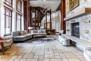 Living room featuring a towering ceiling, stone tile flooring, a fireplace, and stairs