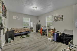 Bedroom featuring light wood-type flooring, a textured ceiling, and an office area