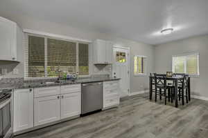 Kitchen featuring light stone counters, stainless steel appliances, white cabinets, and light wood-type flooring
