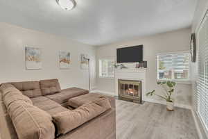 Living area with a fireplace with flush hearth, light wood finished floors, and a textured ceiling