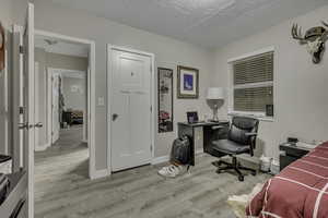 Bedroom featuring light wood-style floors, a textured ceiling, and a desk