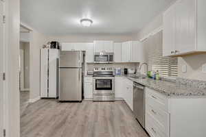 Kitchen featuring stainless steel appliances, white cabinets, light stone countertops, light wood-style floors, and a textured ceiling