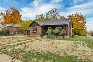Single story home with a porch, roof with shingles, brick siding, a garage, and a chimney
