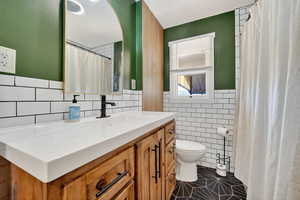 Full bathroom with dark tile patterned flooring, a shower with curtain, vanity, tile walls, and wainscoting