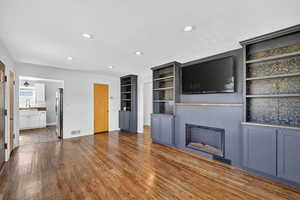 Unfurnished living room with dark wood finished floors, a glass covered fireplace, recessed lighting, and built in features