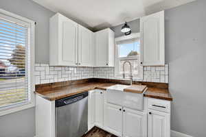 Kitchen featuring tasteful backsplash, stainless steel dishwasher, white cabinetry, and wooden counters