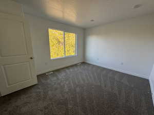 Unfurnished room with a textured ceiling and dark carpet