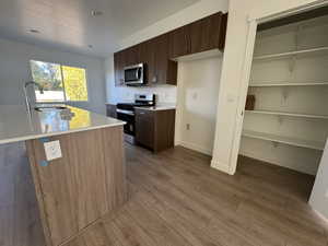 Kitchen featuring dark brown cabinetry, stainless steel appliances, light wood-style floors, modern cabinets, and a kitchen island with sink