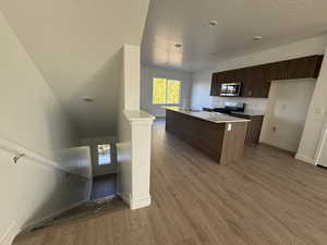 Kitchen with dark brown cabinetry, modern cabinets, a textured ceiling, light wood-style flooring, and stainless steel appliances