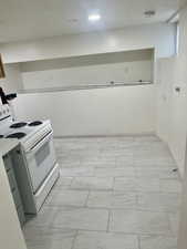 Kitchen with electric stove, a textured ceiling, and light countertops