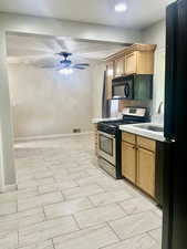 Kitchen with gas stove, light countertops, freestanding refrigerator, a ceiling fan, and brown cabinets