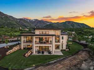 Back of house with stucco siding, a mountain view, a yard, and a patio