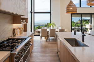 Example of kitchen featuring range with two ovens, light wood-style flooring, decorative light fixtures, modern cabinets, and light brown cabinetry