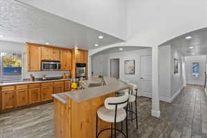 Kitchen featuring recessed lighting, light countertops, a breakfast bar area, arched walkways, and a center island with sink