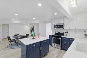 Kitchen with blue cabinetry, appliances with stainless steel finishes, recessed lighting, a center island, and light wood-style flooring