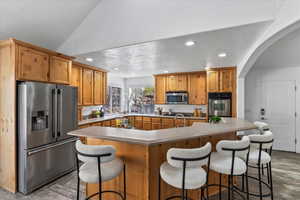 Kitchen with stainless steel appliances, a textured ceiling, recessed lighting, light countertops, and a kitchen breakfast bar