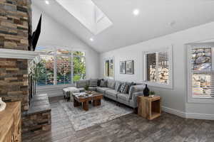 Living room area featuring high vaulted ceiling, dark wood finished floors, a skylight, recessed lighting, and a stone fireplace