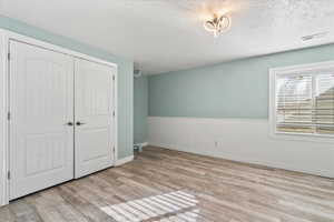 Unfurnished bedroom featuring a wainscoted wall, light wood-style flooring, a closet, and a textured ceiling
