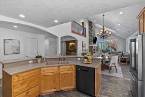 Kitchen with black dishwasher, a textured ceiling, a center island with sink, open floor plan, and light brown cabinetry