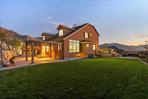 Back of house at dusk featuring a mountain view, a lawn, a patio, and stucco siding