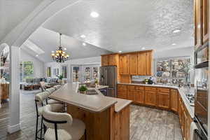 Kitchen featuring brown cabinetry, light countertops, hanging light fixtures, an island with sink, and a textured ceiling