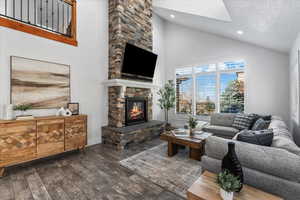 Living room with a fireplace, high vaulted ceiling, wood finished floors and balcony