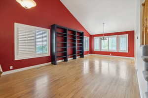 Unfurnished living room with high vaulted ceiling, light wood-type flooring, and a chandelier