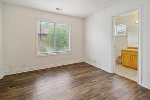 Unfurnished bedroom featuring connected bathroom and dark wood-style flooring
