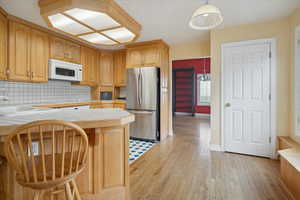 Kitchen with tile countertops, backsplash, freestanding refrigerator, and a peninsula