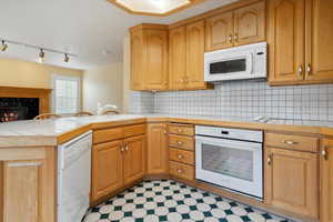 Kitchen featuring white appliances, a fireplace, backsplash, light floors, and a peninsula