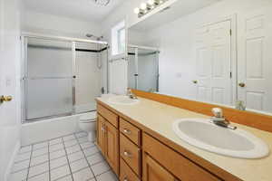 Full bathroom with double vanity, bath / shower combo with glass door, and light tile patterned flooring