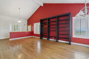 Empty room featuring beamed ceiling, light wood-style flooring, and high vaulted ceiling