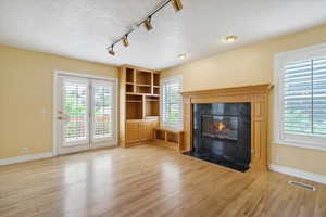Unfurnished living room featuring track lighting, a high end fireplace, light wood finished floors, radiator heating unit, and a textured ceiling