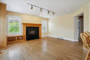 Unfurnished living room featuring track lighting, light wood finished floors, healthy amount of natural light, and a high end fireplace