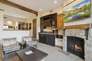 Living room featuring a stone fireplace, beam ceiling, and recessed lighting