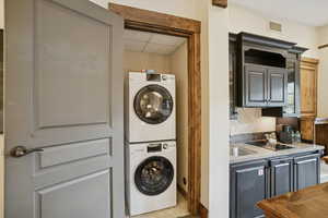 Laundry area with light tile patterned floors, stacked washer and clothes dryer, and a drop ceiling