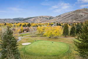View of home's community with an area to practice putting, a yard, a mountain view, golf course view, and view of wooded area