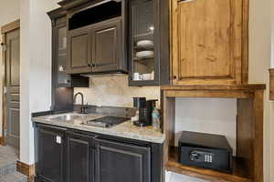 Kitchen with light stone counters, decorative backsplash, glass insert cabinets, and black electric stovetop