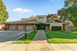 View of front of home with driveway, an attached garage, brick siding, and a chimney