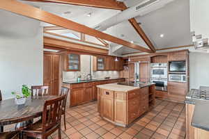 Kitchen featuring open shelves, appliances with stainless steel finishes, tasteful backsplash, light tile patterned floors, and a center island with sink