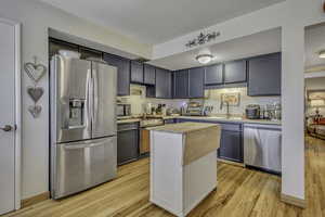 Kitchen with appliances with stainless steel finishes, light wood-style flooring, butcher block counters, and a center island