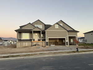 Craftsman-style house with covered porch, board and batten siding, a shingled roof, and a garage