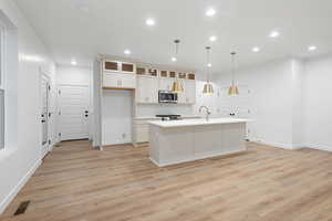 Kitchen with a center island with sink, recessed lighting, tasteful backsplash, light wood finished floors, and glass insert cabinets