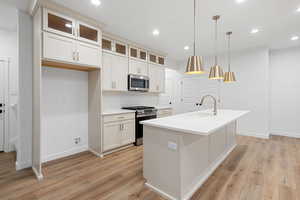 Kitchen featuring tasteful backsplash, appliances with stainless steel finishes, glass insert cabinets, decorative light fixtures, and light wood finished floors
