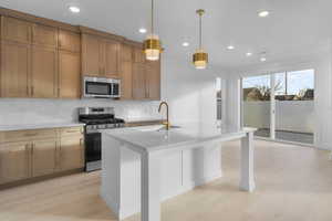 Kitchen featuring appliances with stainless steel finishes, pendant lighting, light stone counters, a kitchen island with sink, and recessed lighting