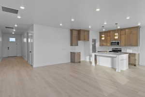 Kitchen with open floor plan, brown cabinets, appliances with stainless steel finishes, decorative light fixtures, and a breakfast bar