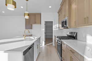 Kitchen featuring stainless steel appliances, light stone counters, hanging light fixtures, recessed lighting, and a kitchen island with sink